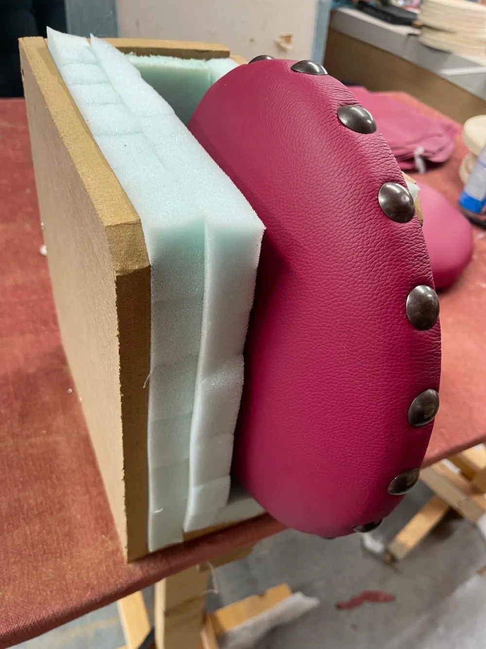 A stud-trimmed burgundy leather seat pad in progress on its foam and board base