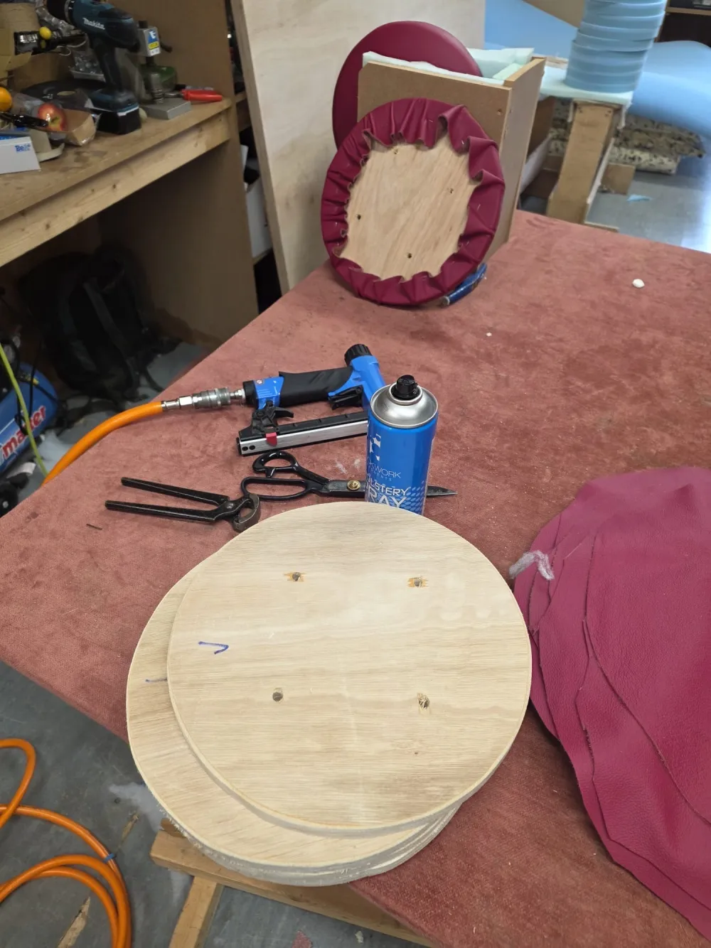 Round seat bases and burgundy leather being cut and prepared on the workshop bench