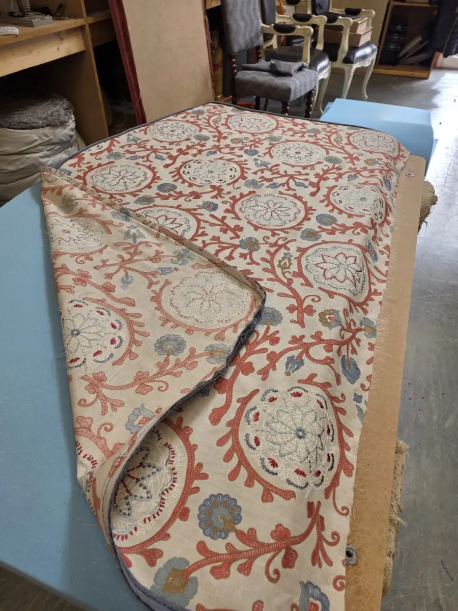 A roll of terracotta and blue suzani embroidered fabric on the workbench