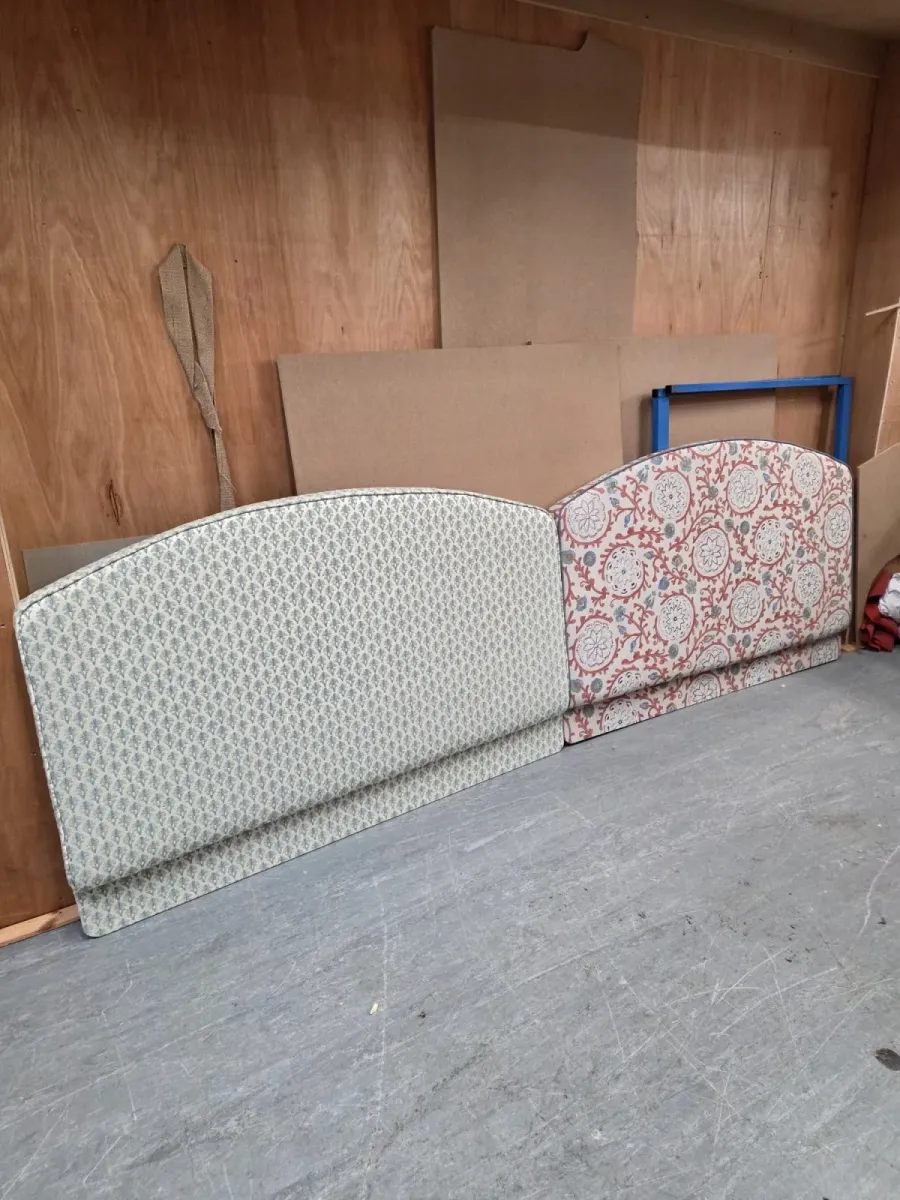 A pair of upholstered headboards, one in a green sprig print and one in a terracotta suzani fabric