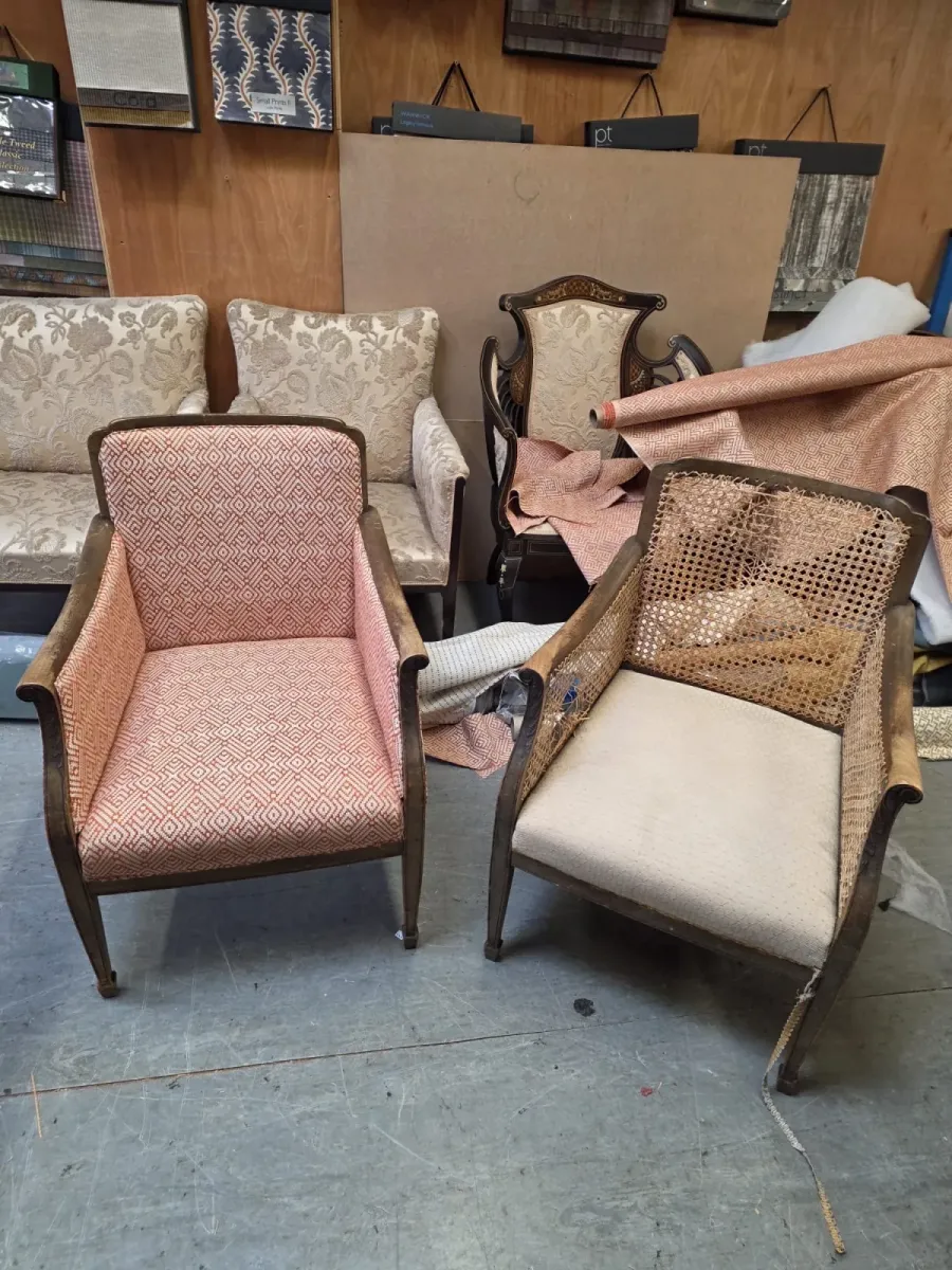 A reupholstered diamond-weave armchair beside a cane-sided bergère awaiting restoration in the workshop