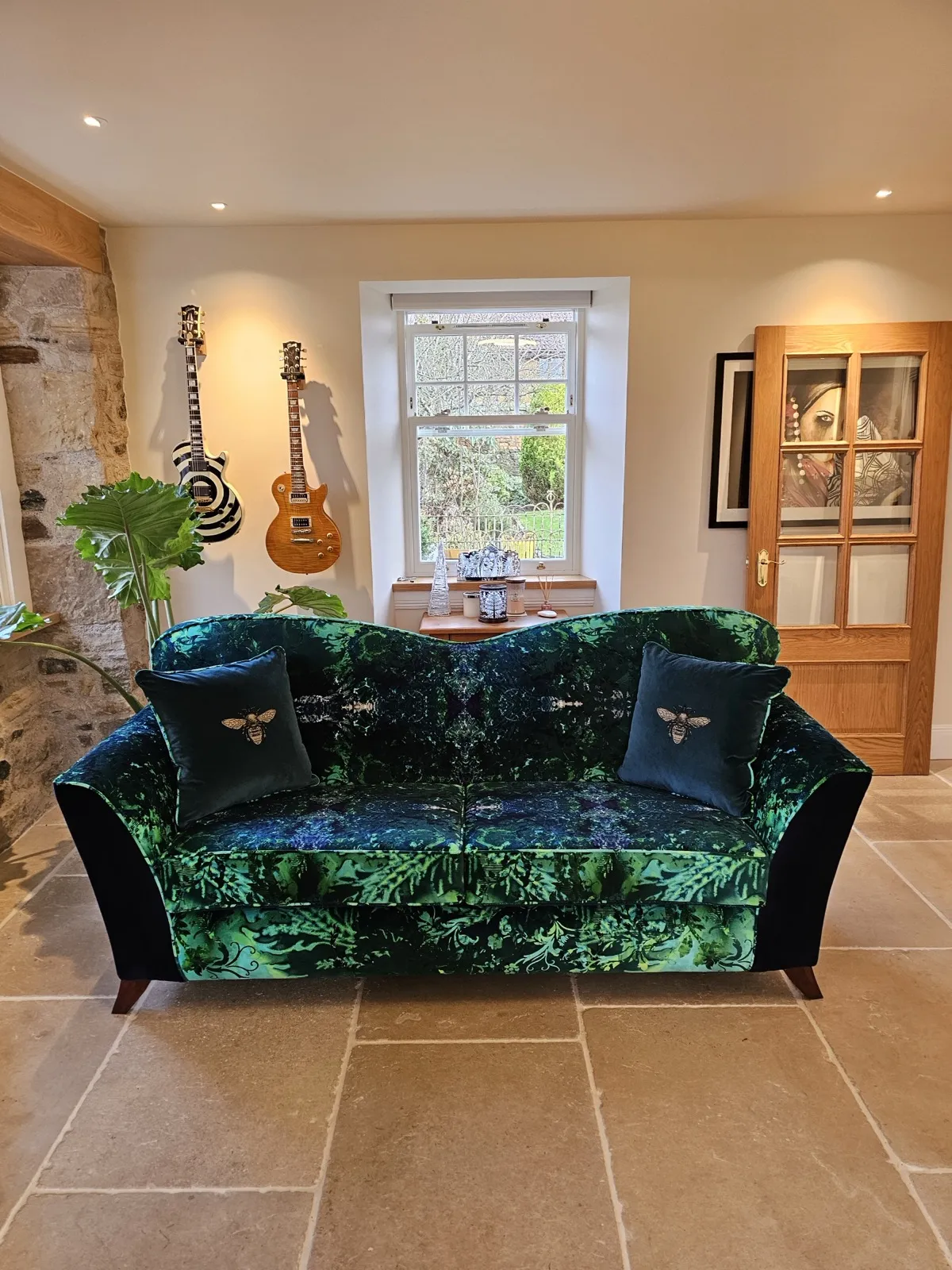A sofa reupholstered in a green botanical velvet, styled in a stone-floored room