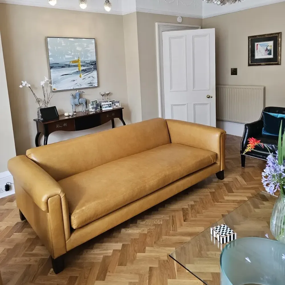 A mid-century sofa reupholstered in tan aniline leather, set in a period room